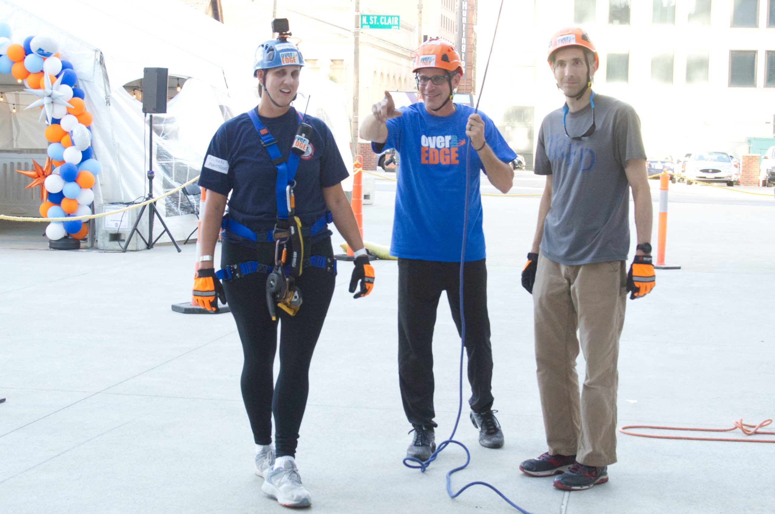 Three people in helmets and harnesses, standing on a city street, smiling.