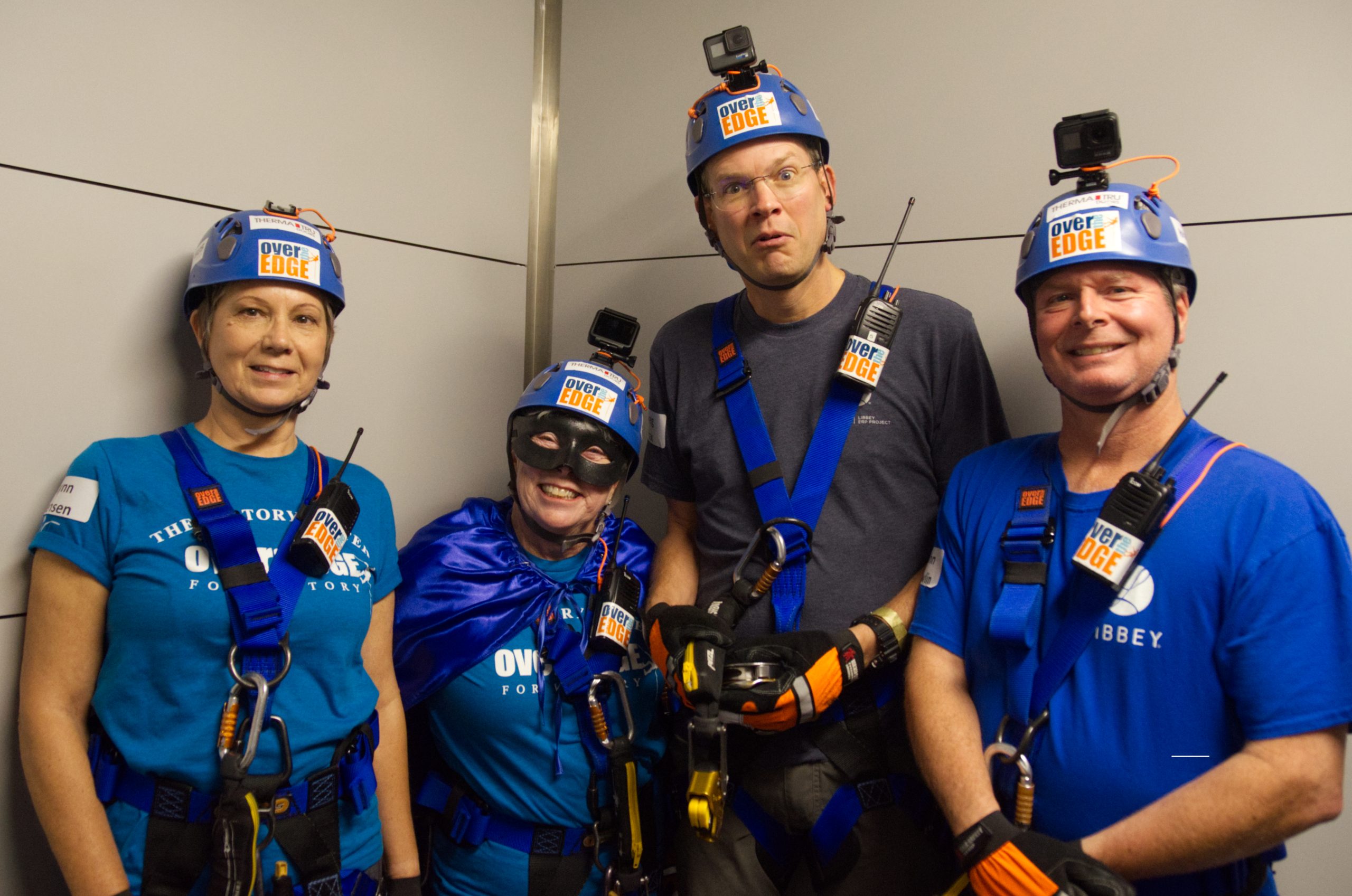 Group of four people in helmets and harnesses smiling indoors.