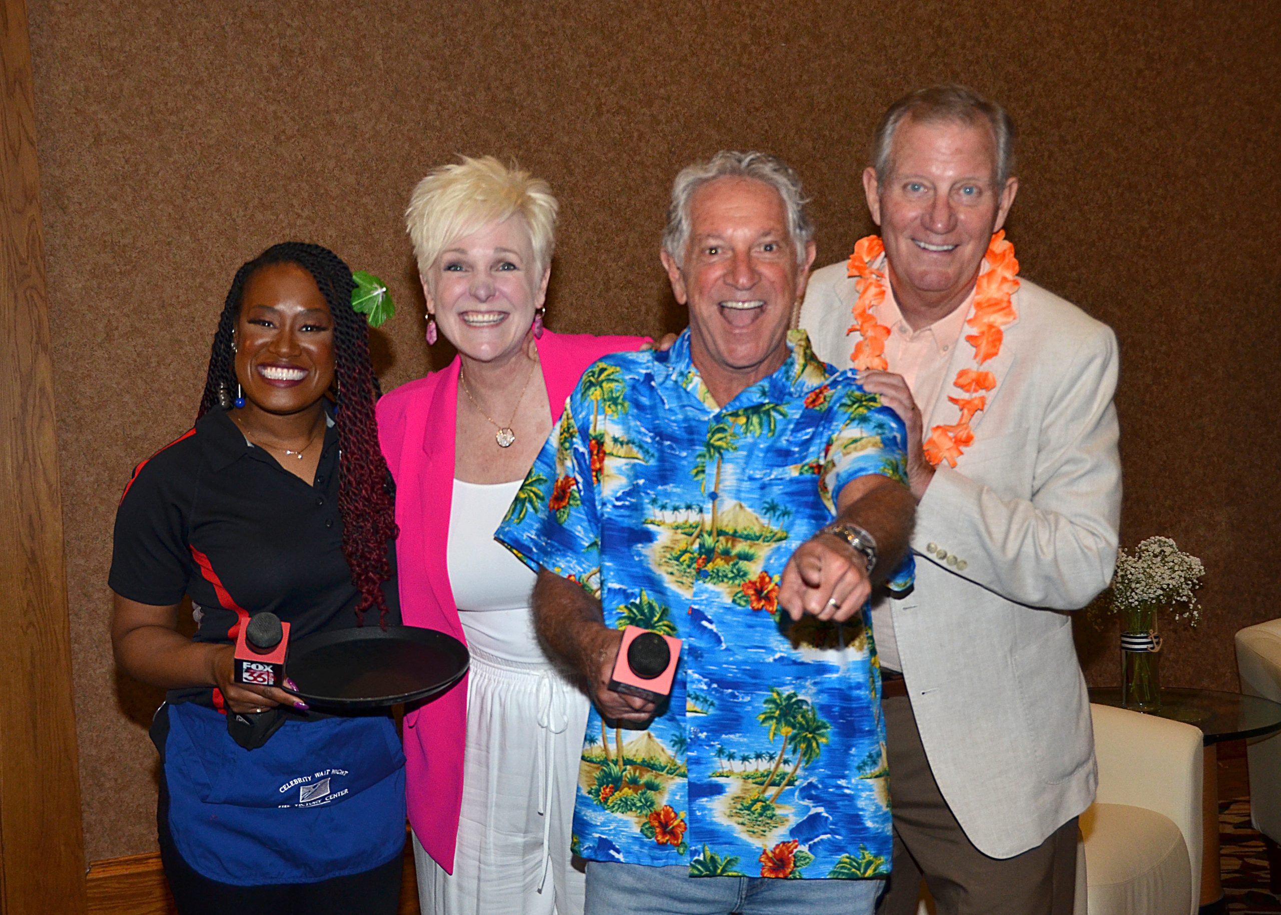 Four people smiling, two holding timers, one in a floral shirt and another with a lei.