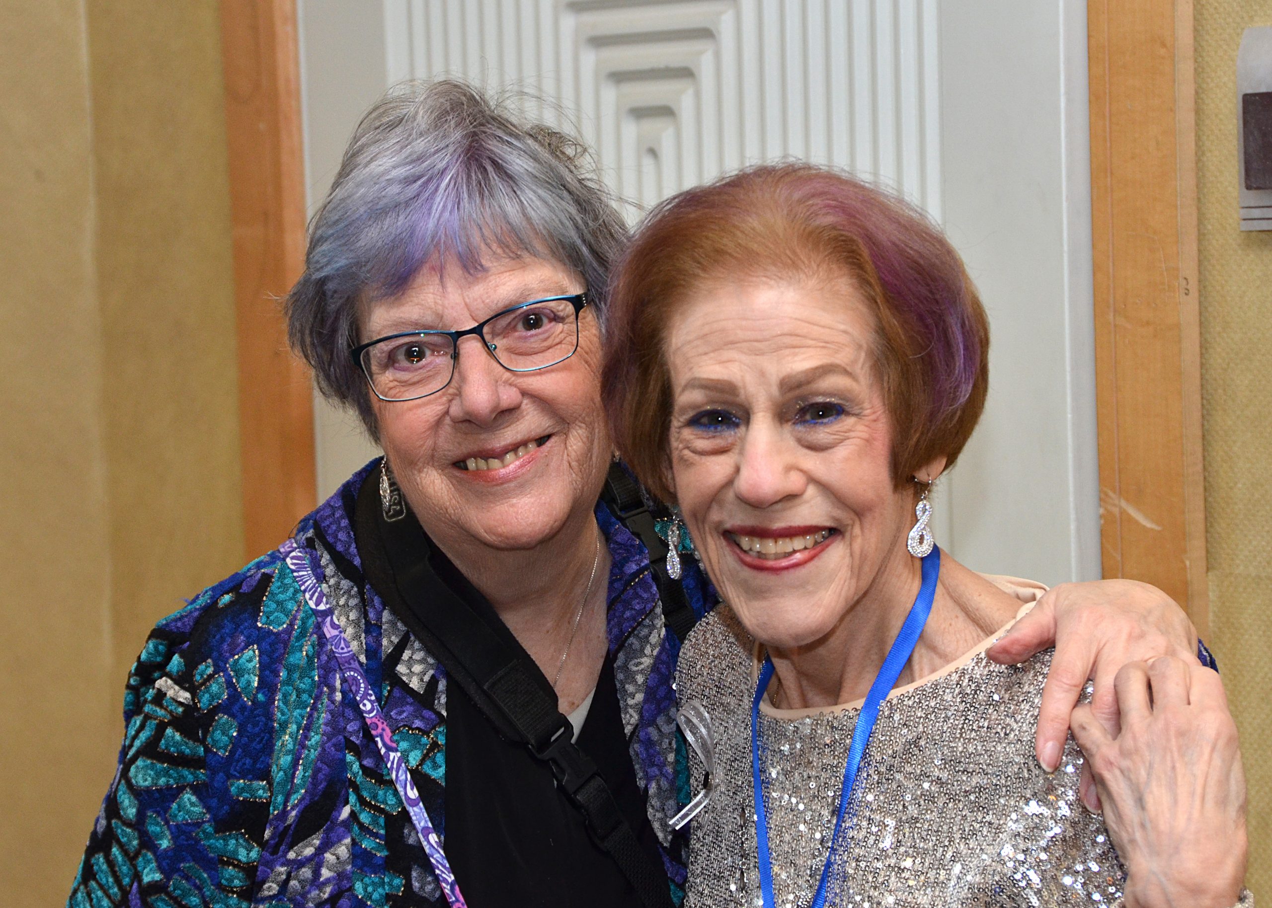 Two elderly women smiling, embracing at an event.