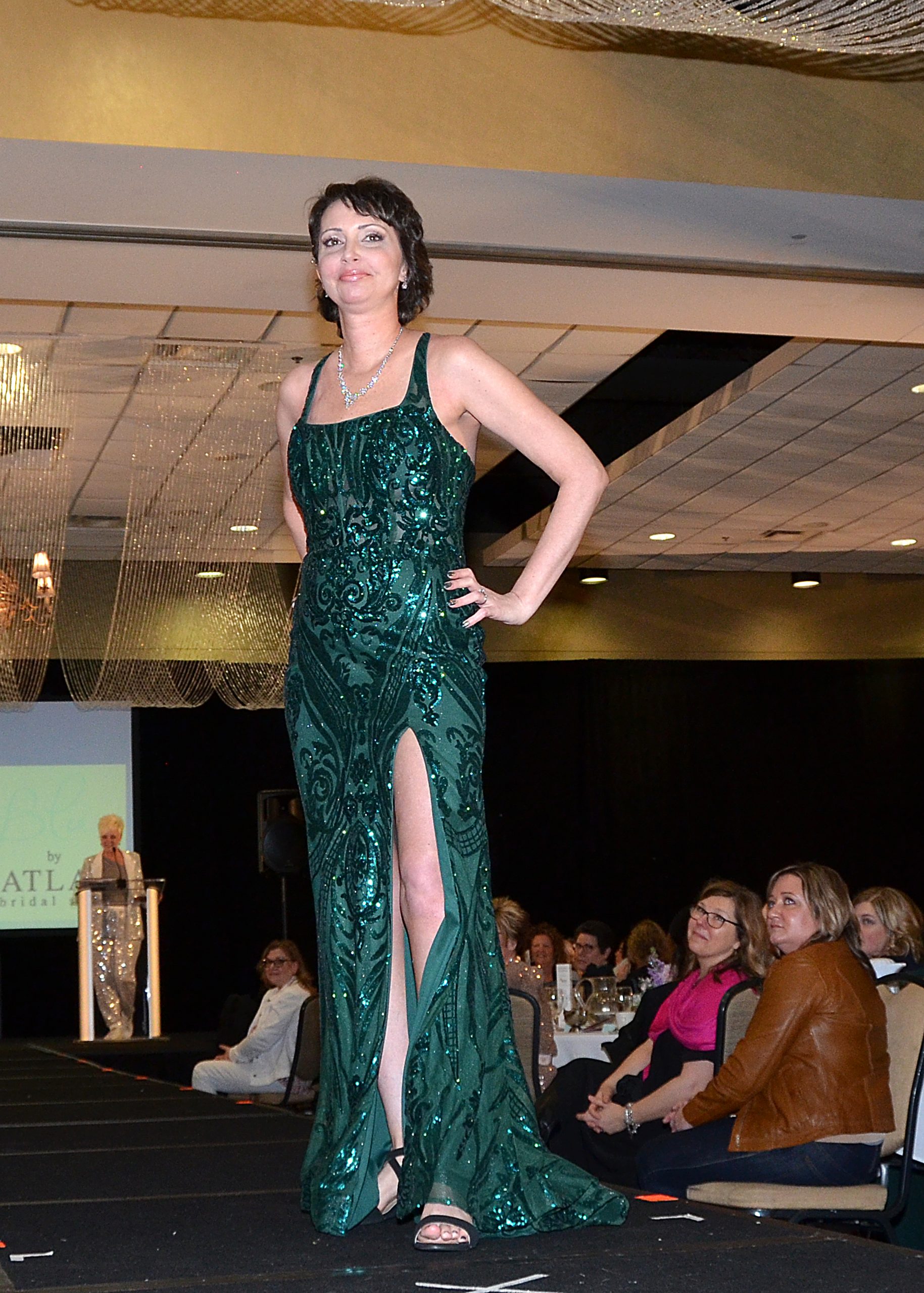 Model in a green gown walking confidently on a fashion runway.