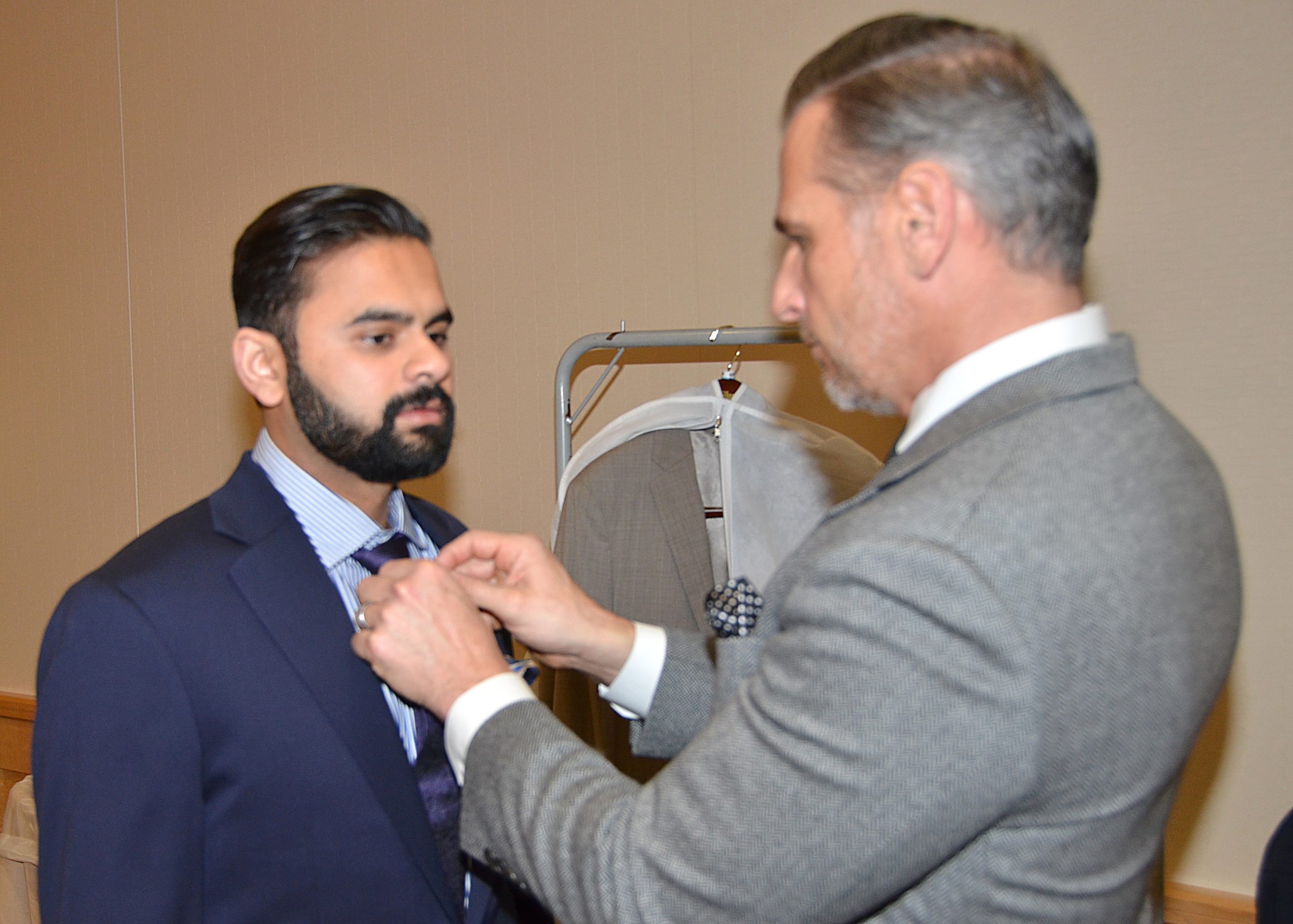 Man adjusts another man's tie in a formal setting.