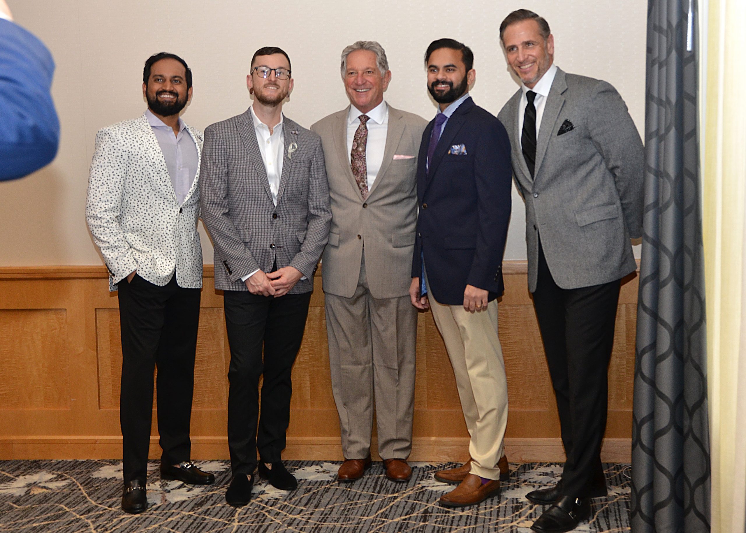Five men in suits smiling, posing indoors.