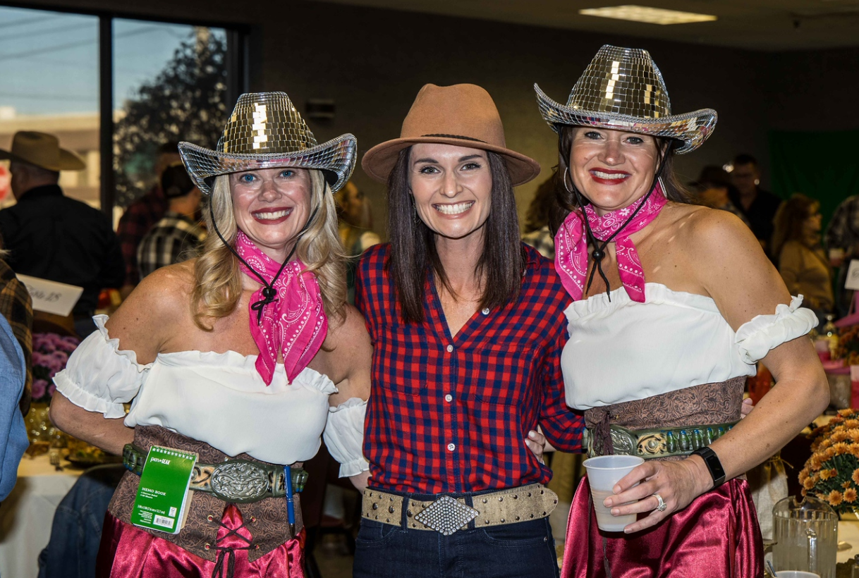 Three women in cowboy hats, smiling indoors.