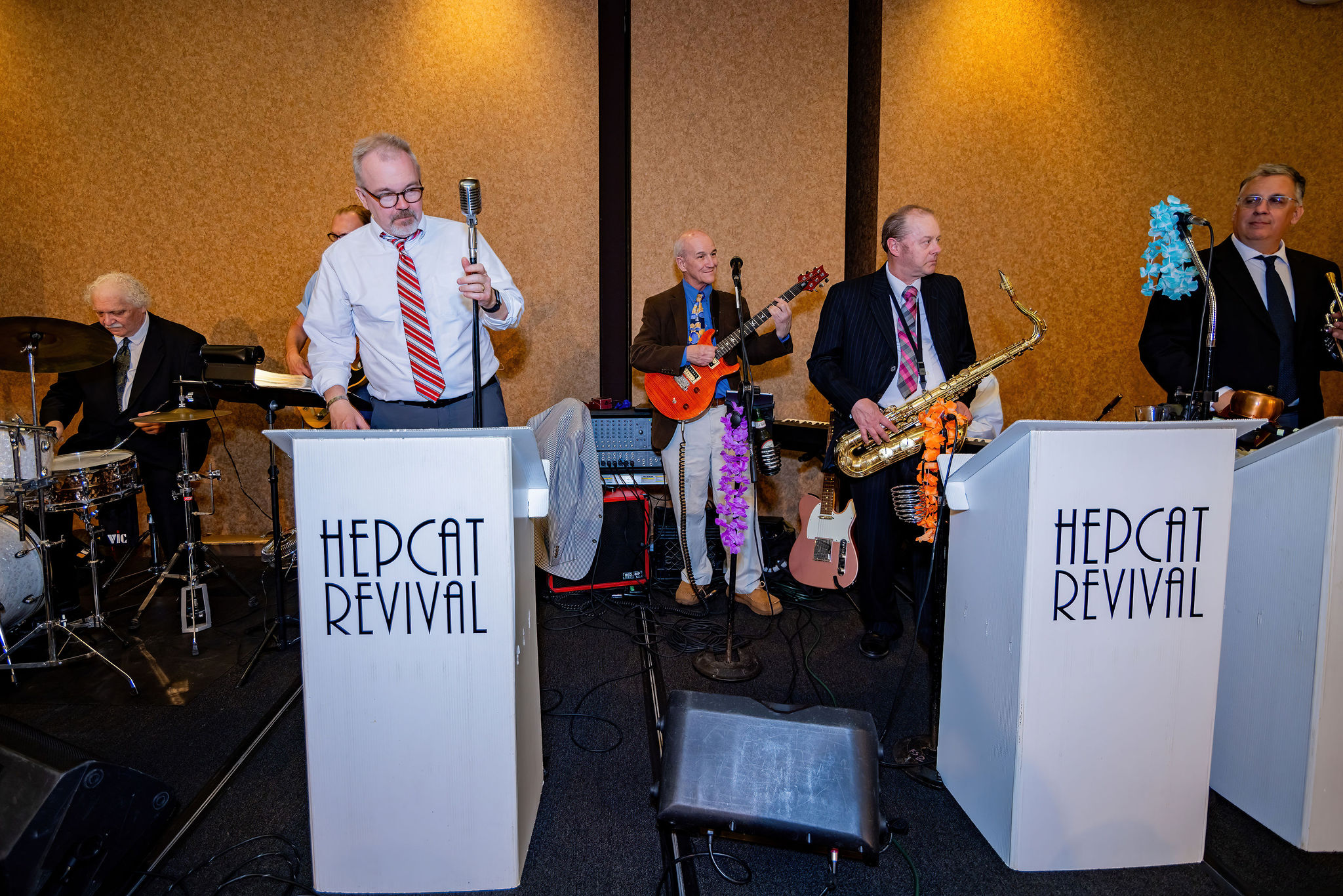 Band performing with instruments, including drums, saxophone, and guitar, in a lively setting.