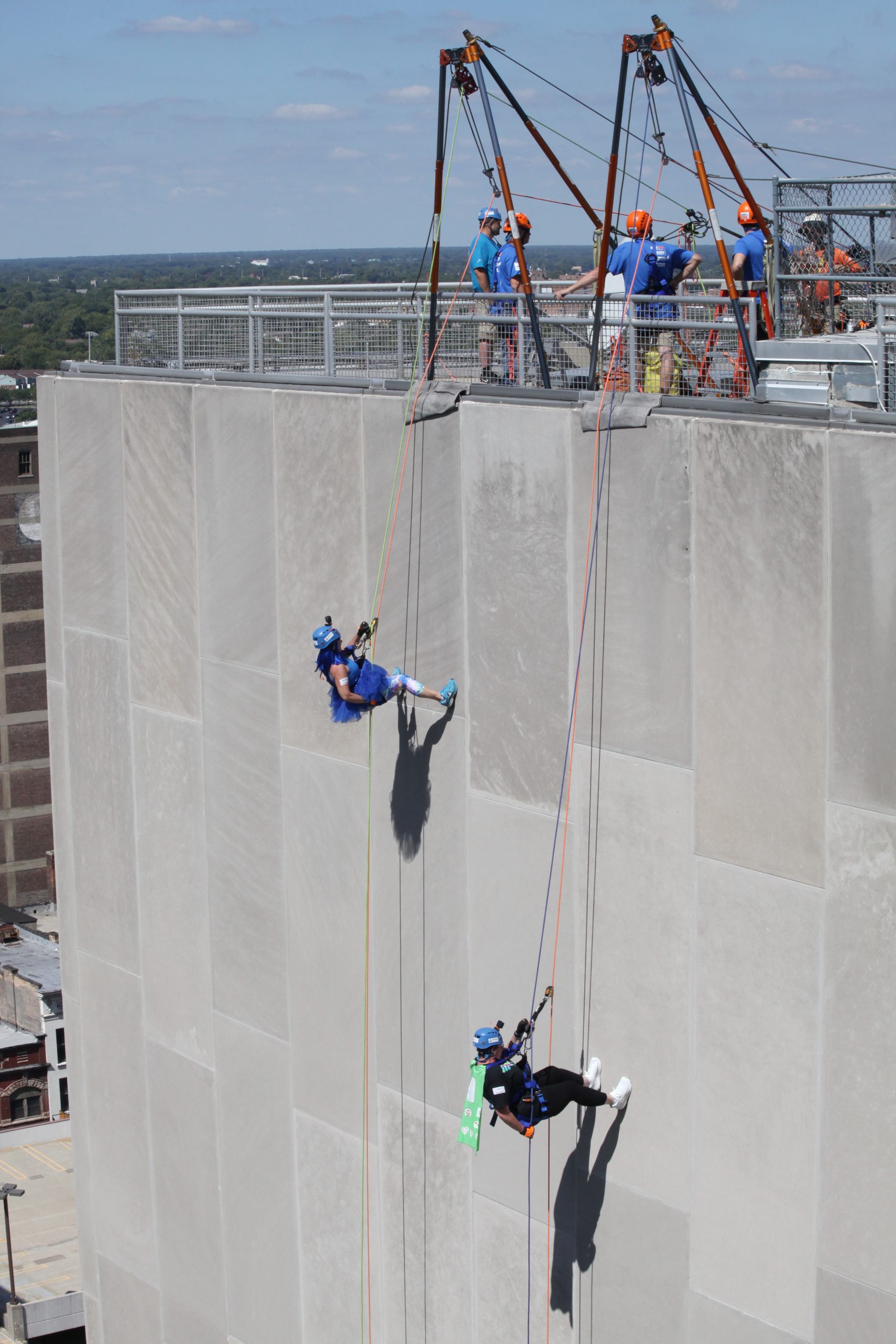 People rappelling down a tall building, with others watching at the top.