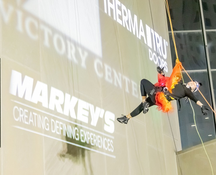 Person in costume rappelling down a building with colorful lights.