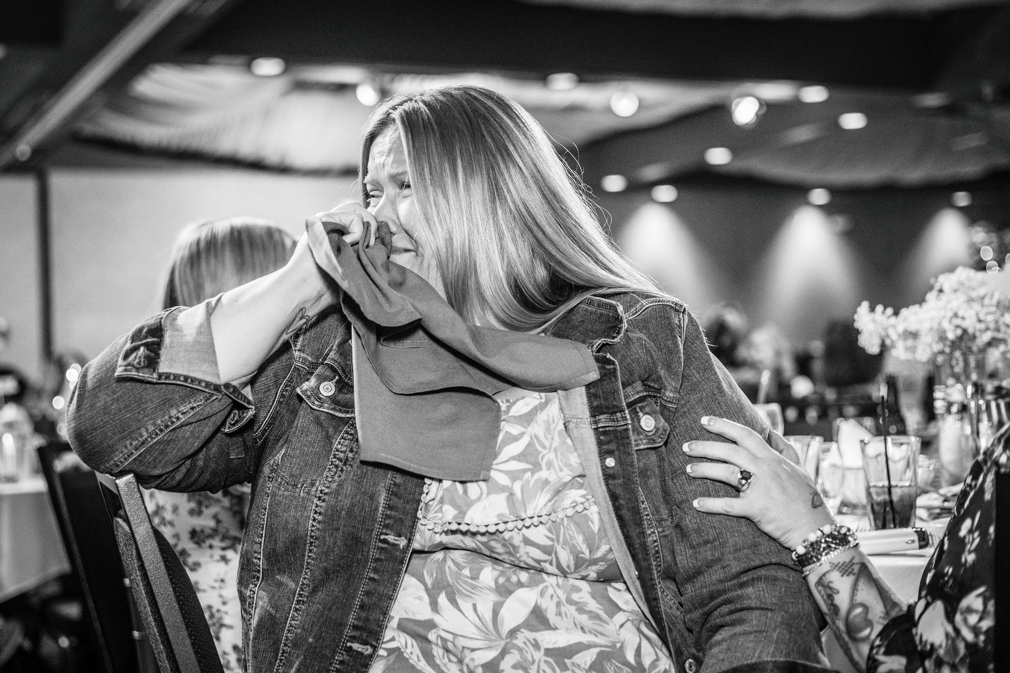 Woman in a denim jacket smiling and wiping tears at an event.