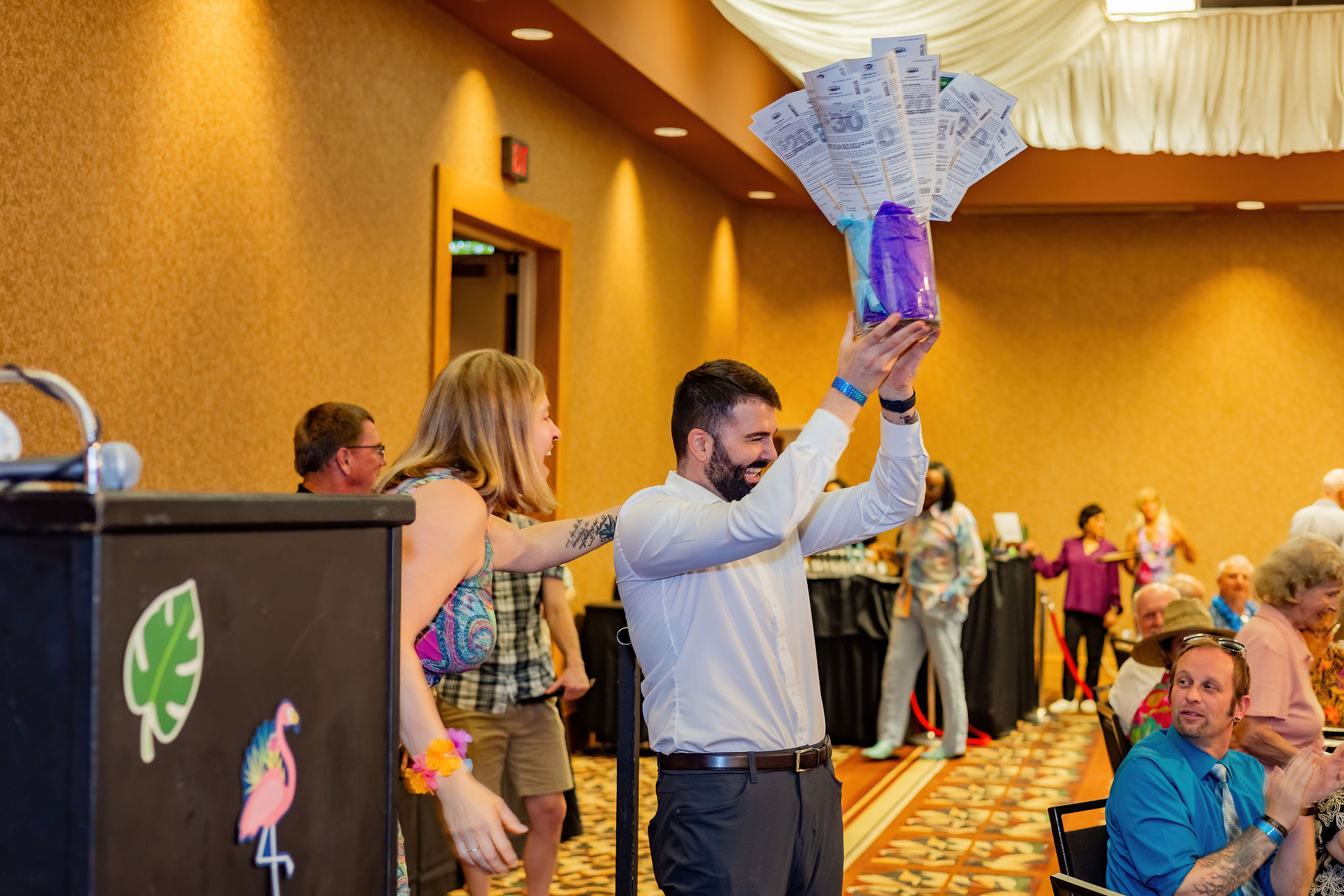 Man holding a purple gift basket aloft at an indoor event with people in the background.