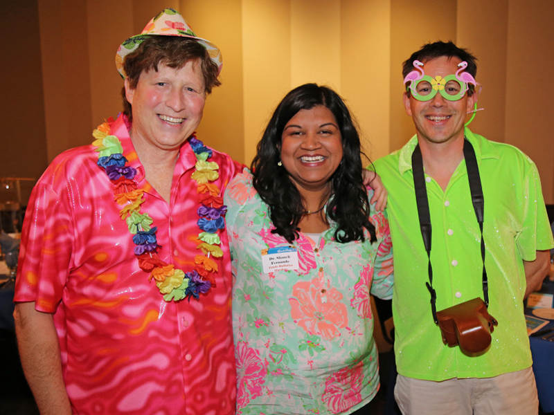 Three people in colorful tropical shirts smiling at an event.