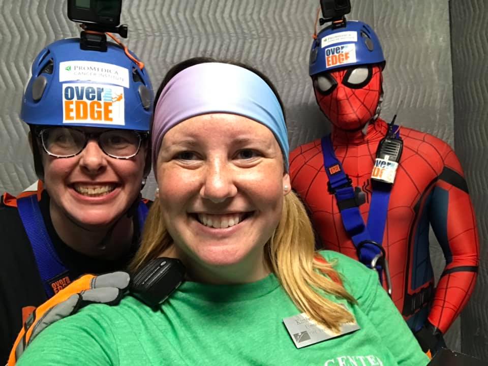 Three people smiling, one in a Spider-Man costume, wearing helmets and harnesses.