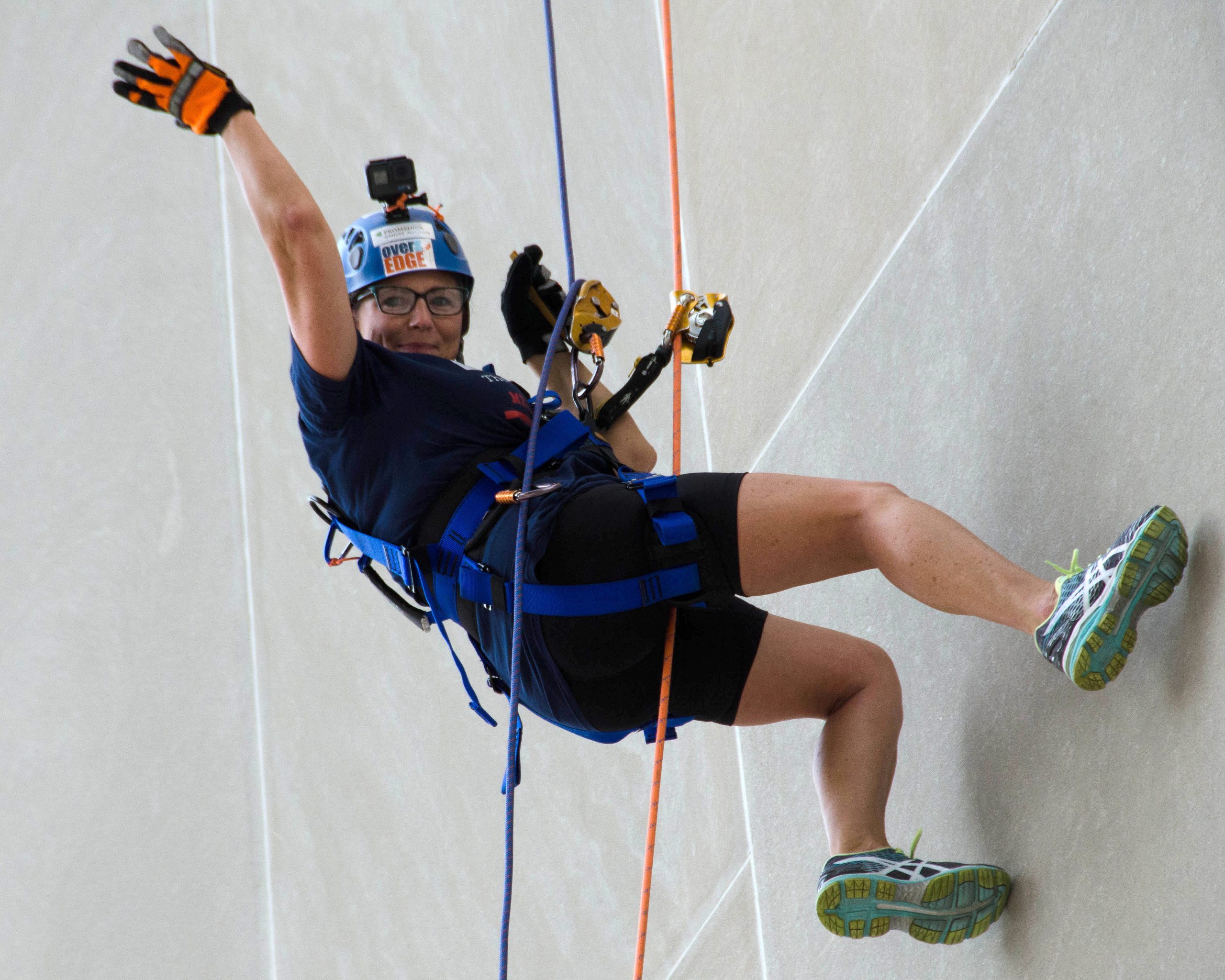 Rock climber ascending a wall, smiling, wearing safety gear and helmet.