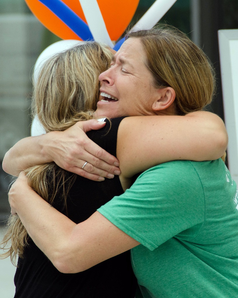 Two women embrace tightly, one looking emotional.