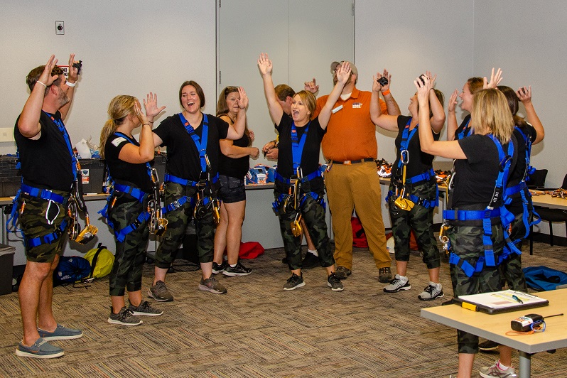 Group celebrating in room, wearing harnesses and casual attire.
