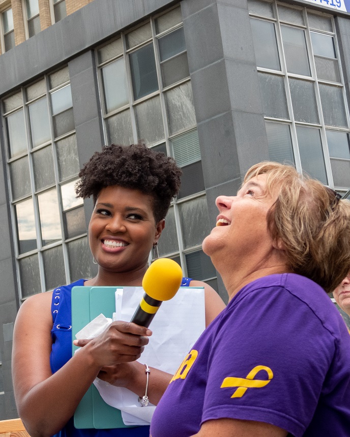 Woman with microphone interviewing a smiling person outdoors.