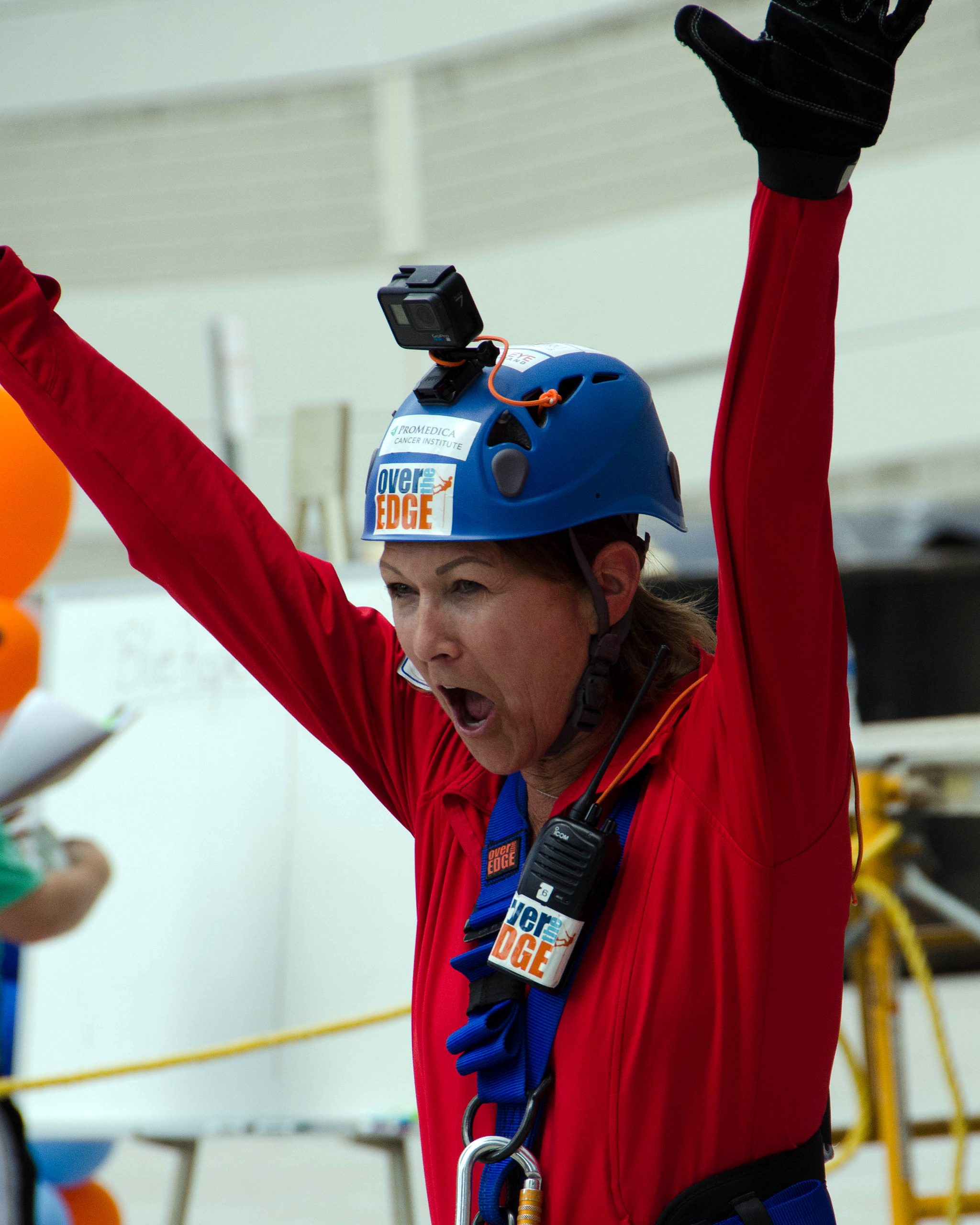 Woman in blue helmet and red suit celebrates with arms raised.