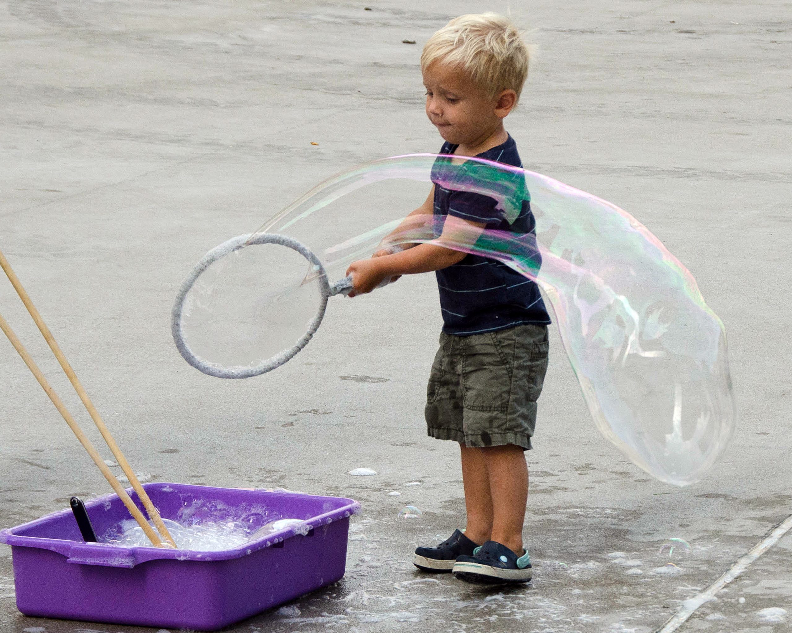 Young child making large bubble with a hoop outdoors.