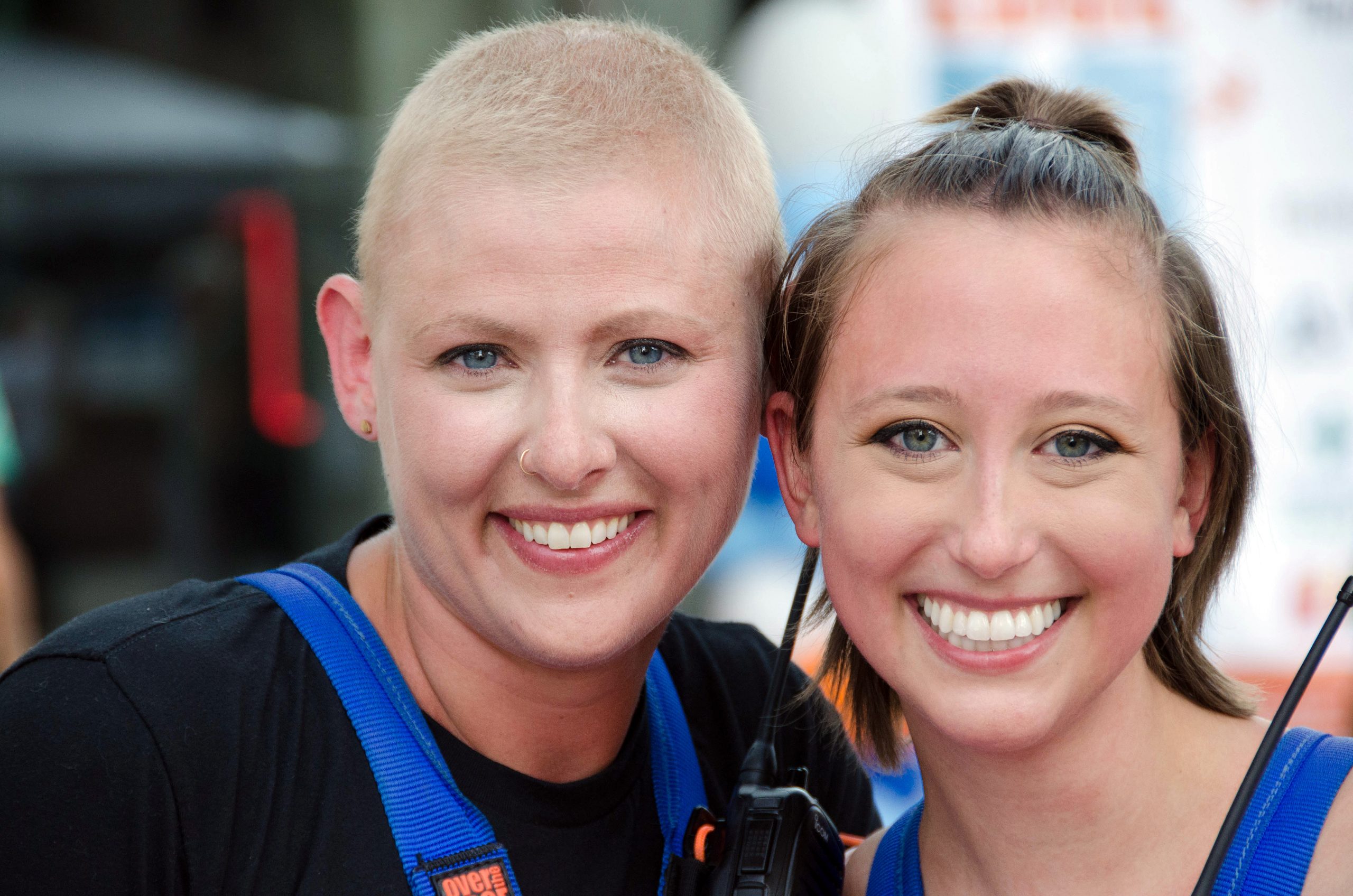 Two people smiling in blue outfits, outdoors, close together.