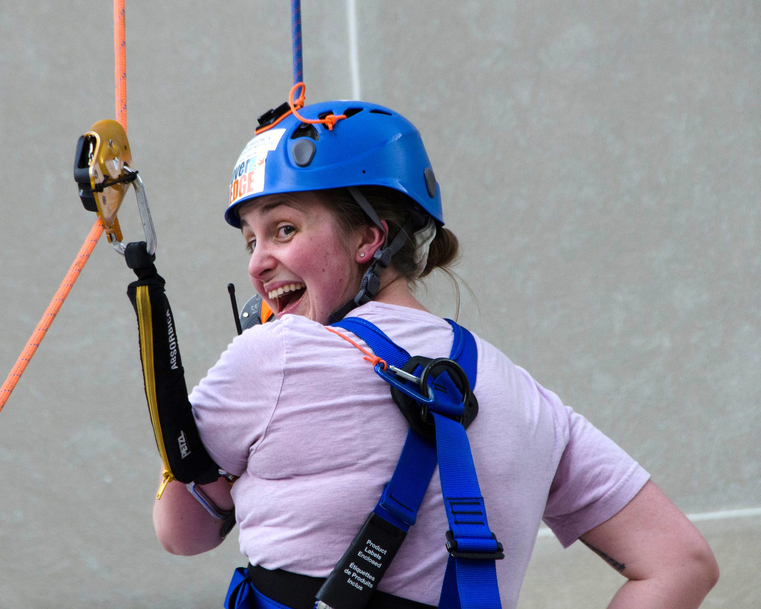Woman with a blue helmet climbing, smiling at the camera.