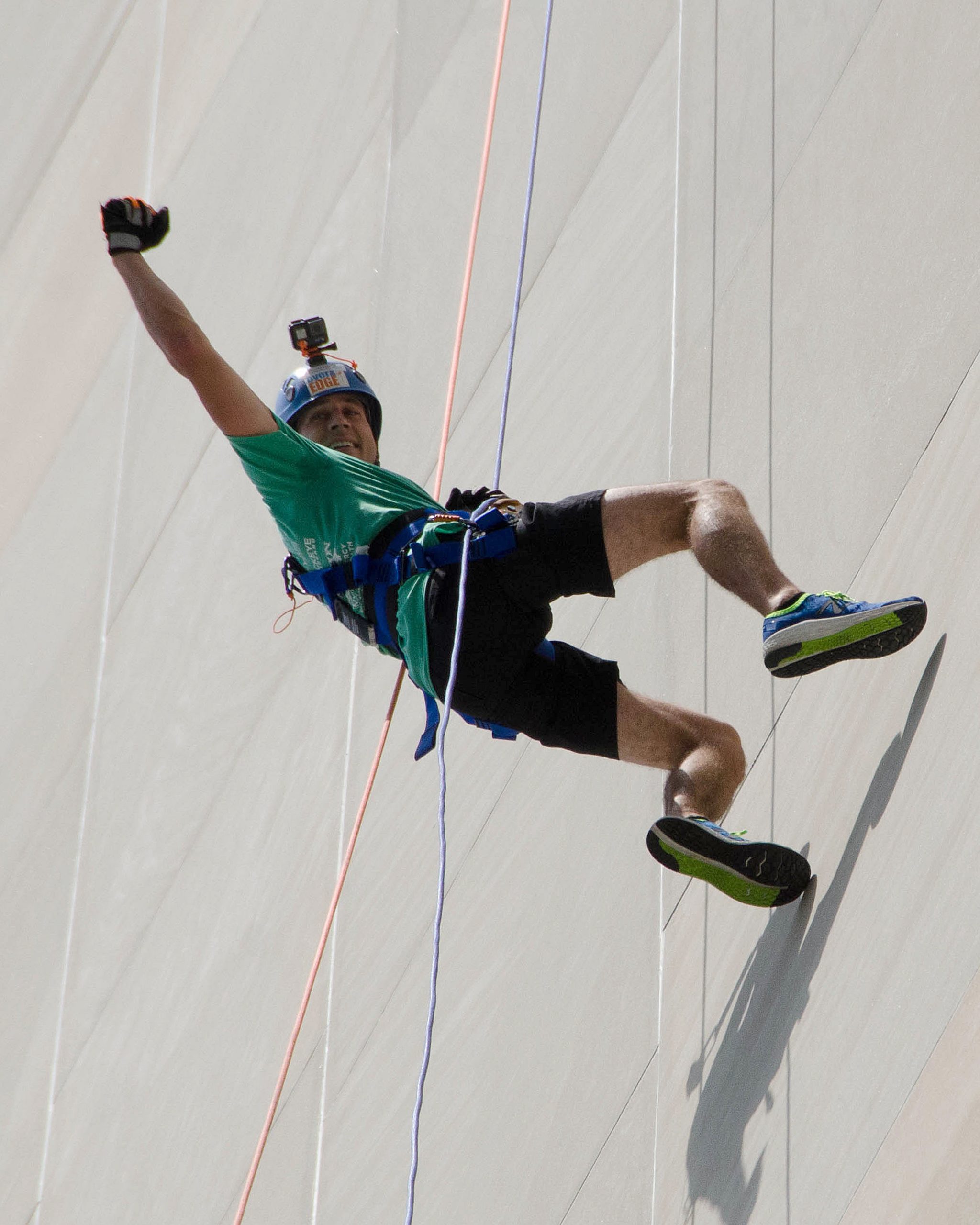 Man in helmet and harness joyfully rappels down a tall wall.