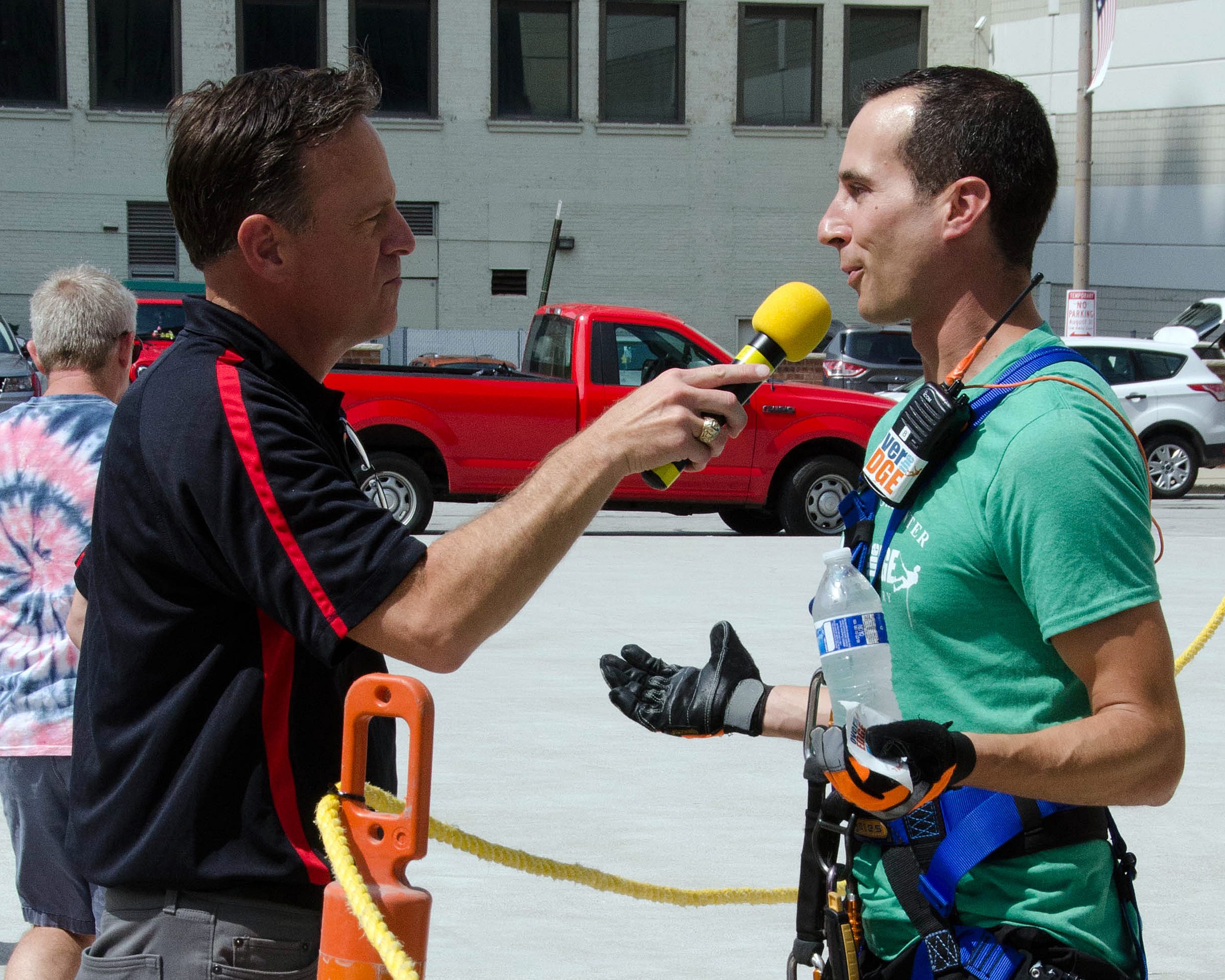A man in a green shirt being interviewed by another holding a yellow microphone.