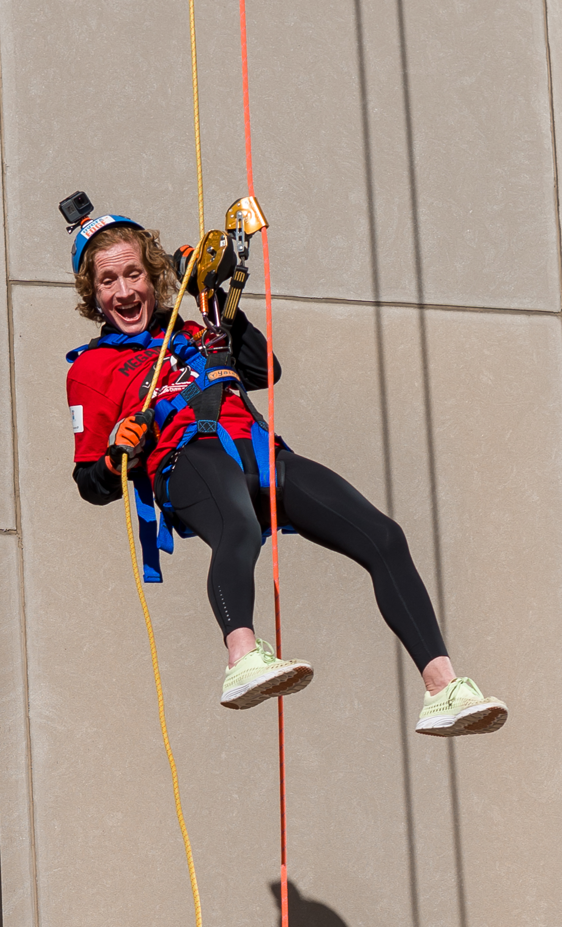 Person joyfully rappelling down a building in colorful gear.