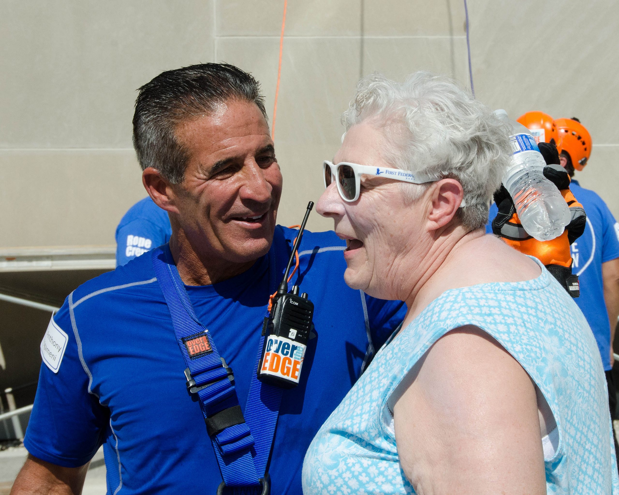 Man and woman smiling, wearing blue outfits and safety harnesses.