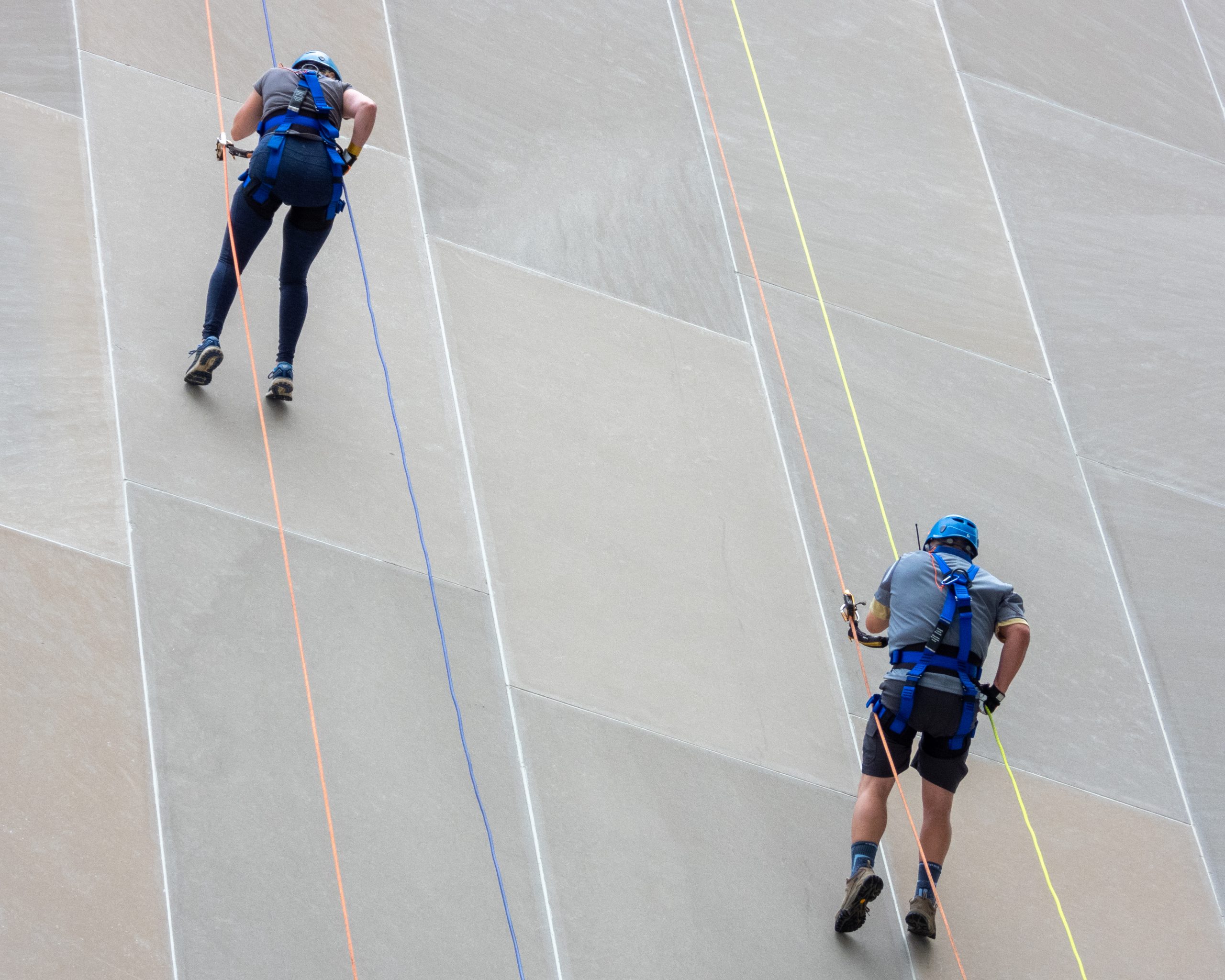 Two people rappelling down a building, wearing helmets and harnesses.