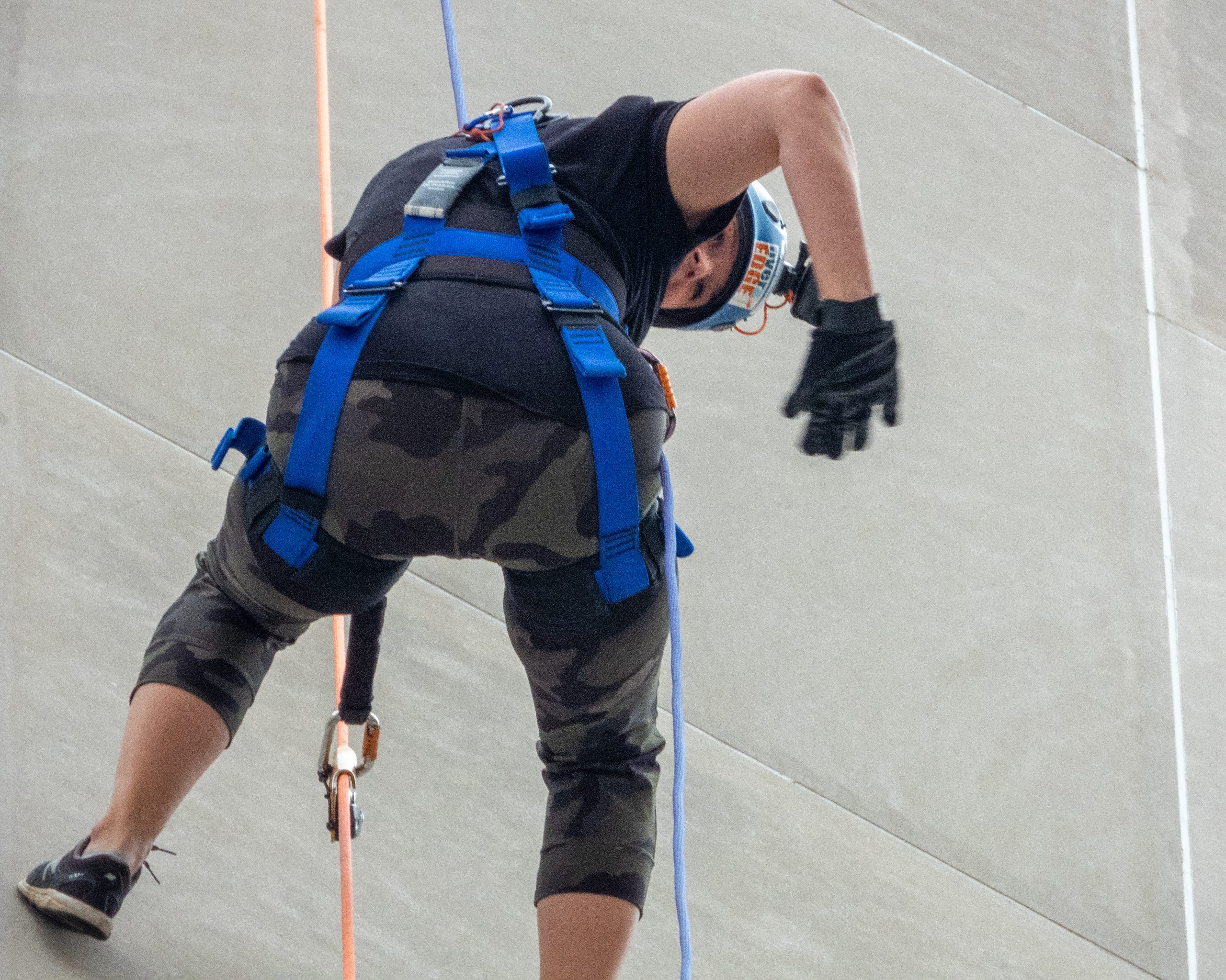 Climber in gear ascending a rope on a concrete wall.