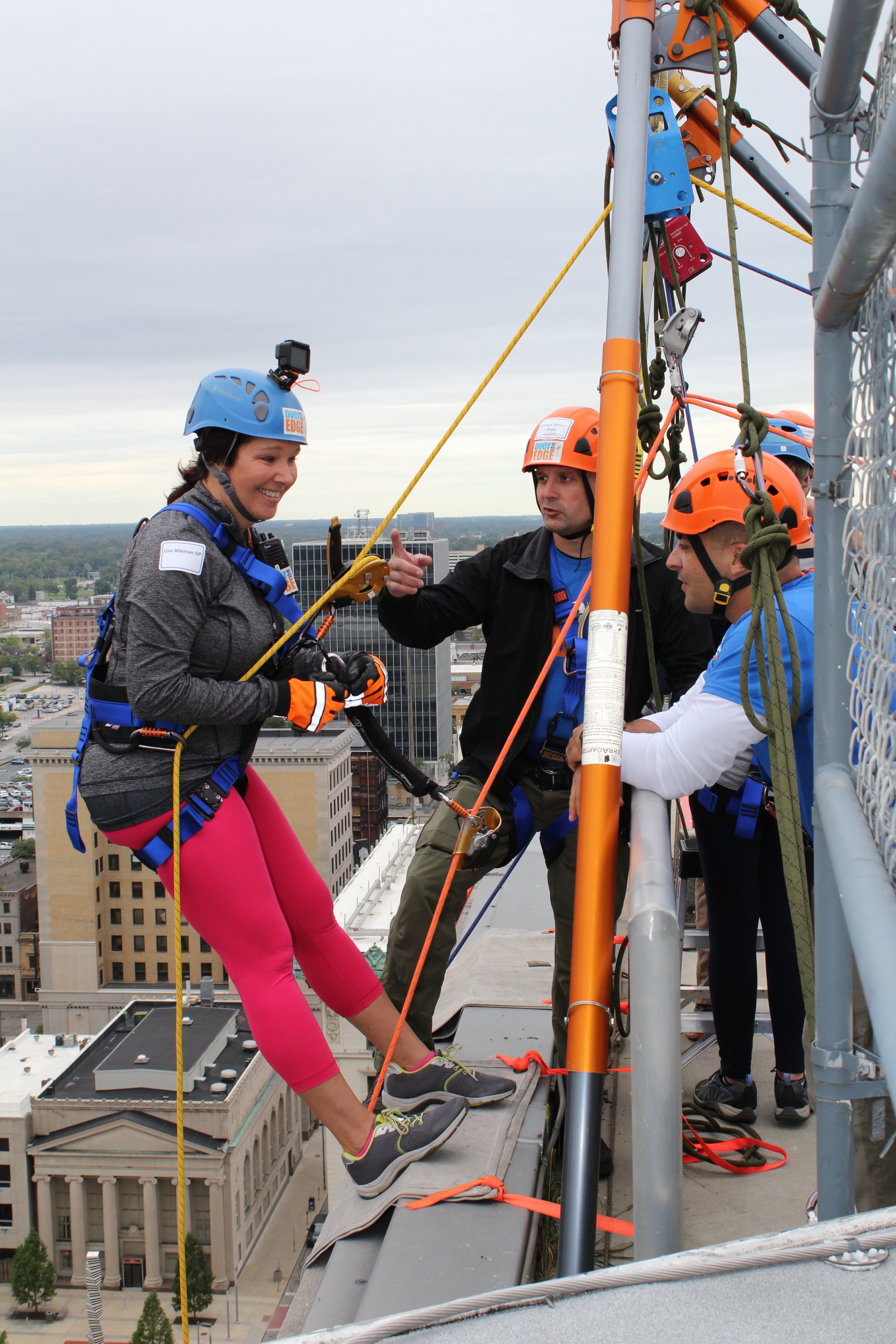 Woman in pink pants prepares to rappel down a building's side.