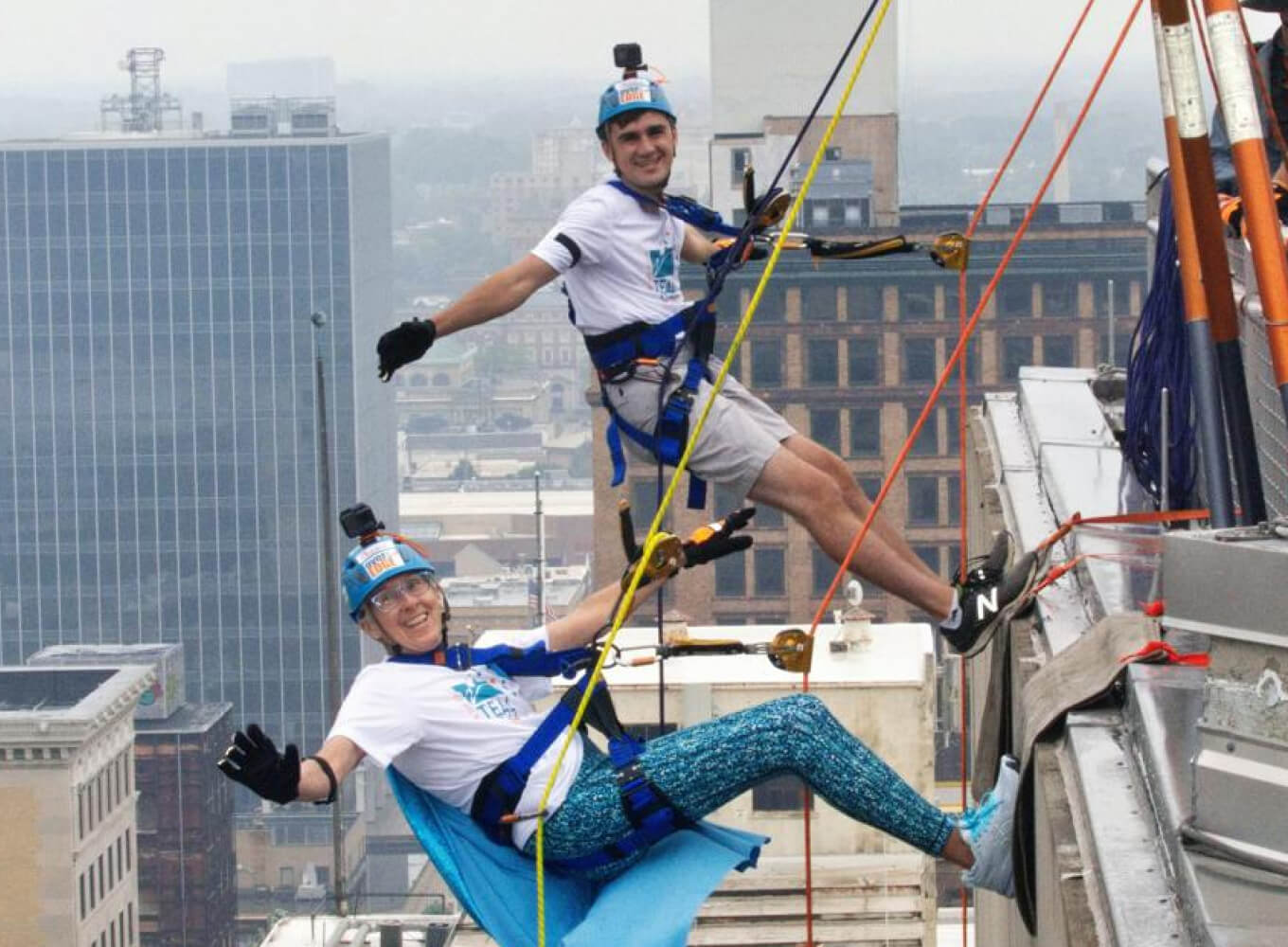 Two People Hanging Over the Edge of a Building