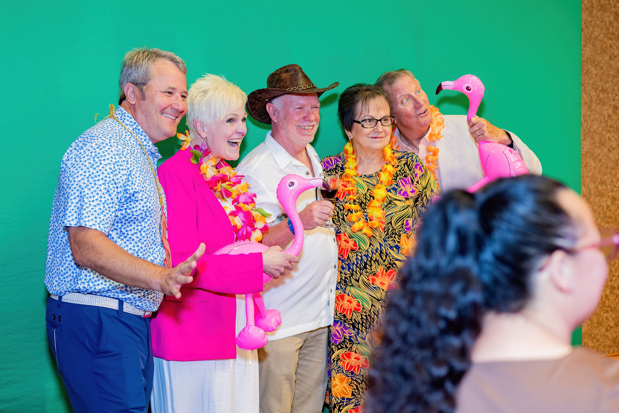 Group of five people smiling with flamingo props, colorful and festive attire.