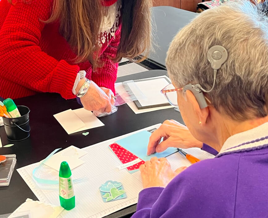 Two women crafting with colored paper and glue sticks at a table.