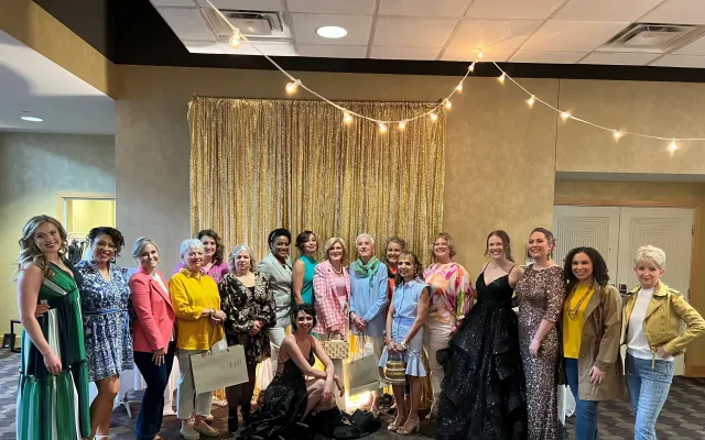 A group of women posed indoors in colorful outfits, with string lights above.