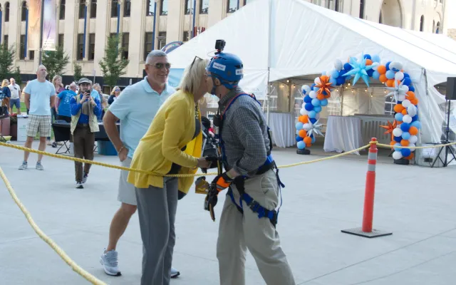 Man in climbing gear and helmet kisses woman in yellow outdoors.