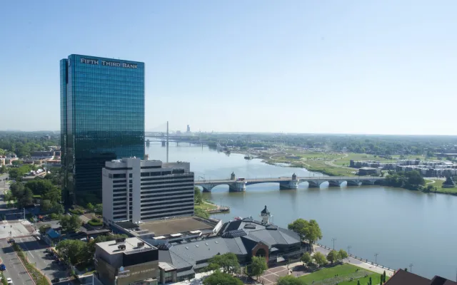 Cityscape with tall glass building, river, and bridge on a clear day.
