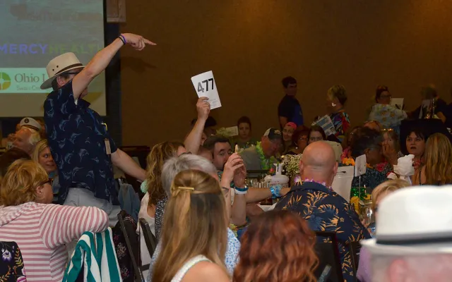 Crowd at an indoor event, one person raising a card.