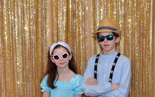 Two children in colorful outfits and sunglasses against a shimmering golden backdrop.