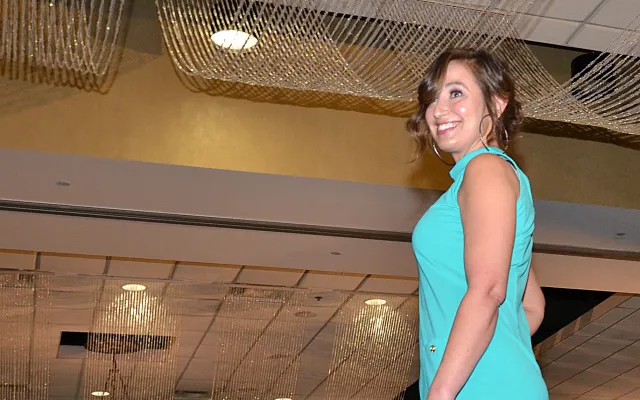 Model in turquoise dress on runway in elegant event setting.