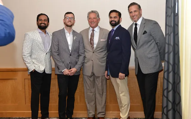 Five men in suits smiling, posing indoors.
