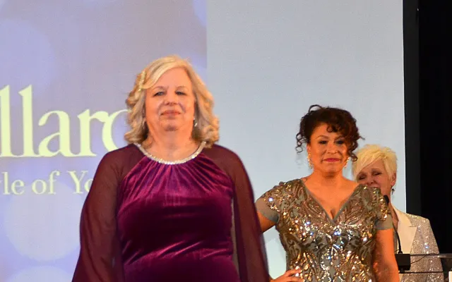 Woman in purple velvet dress on stage, two women in sparkly dresses behind her.