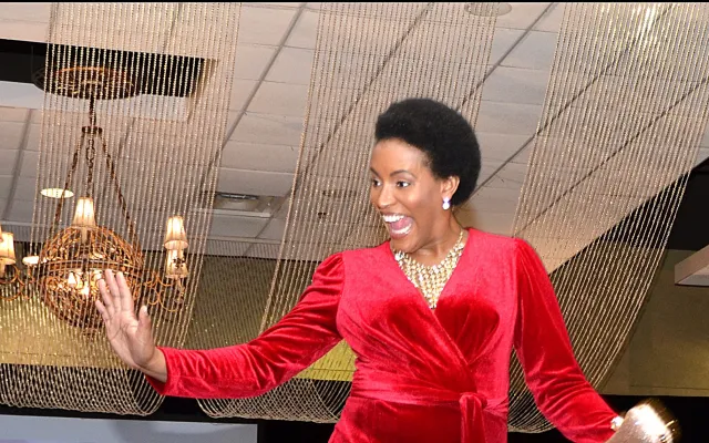 Model in red jumpsuit walks on runway, audience watches.