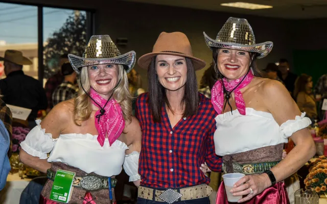 Three women in cowboy hats, smiling indoors.