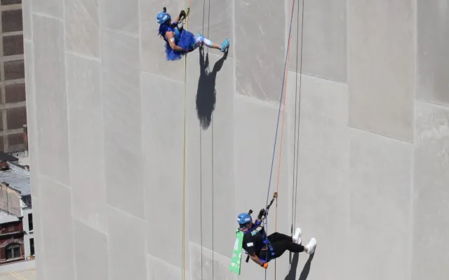People rappelling down a tall building, with others watching at the top.