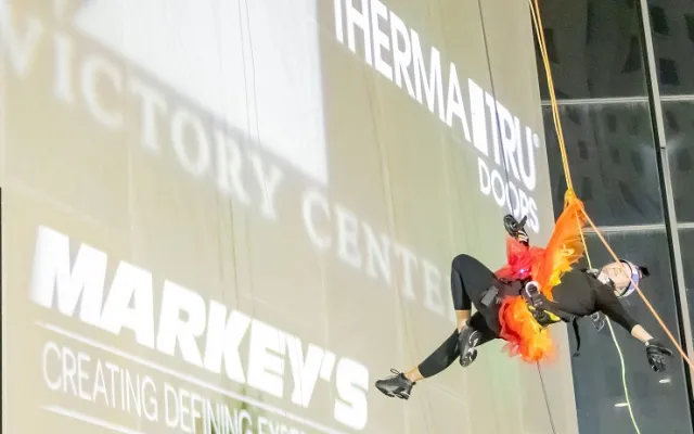 Person in costume rappelling down a building with colorful lights.