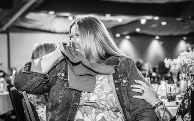 Woman in a denim jacket smiling and wiping tears at an event.