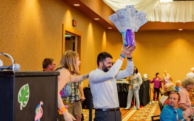 Man holding a purple gift basket aloft at an indoor event with people in the background.