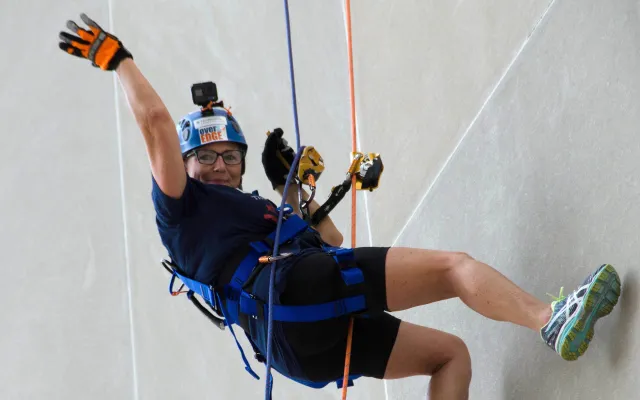 Rock climber ascending a wall, smiling, wearing safety gear and helmet.