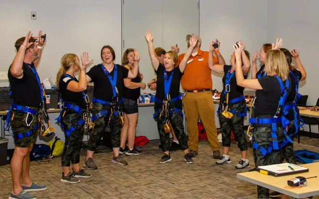 Group celebrating in room, wearing harnesses and casual attire.