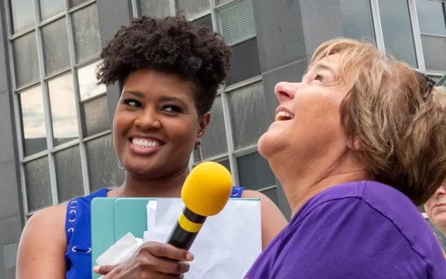 Woman with microphone interviewing a smiling person outdoors.